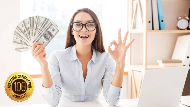 Woman holding money and making an 'ok' sign in a home office setting with a laptop.