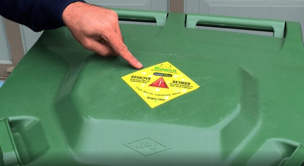 A green container with a yellow removal label is being pointed to by a hand.